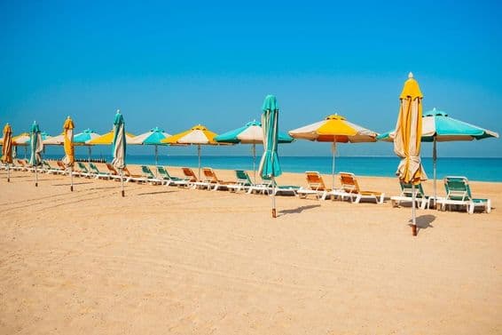 Plage publique de Dubaï, rivage sablonneux, transats et mer bleue.