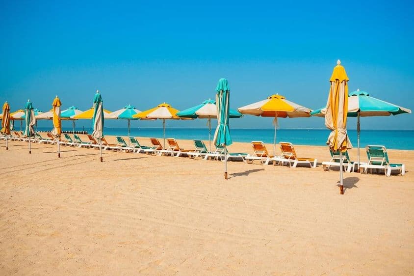 Plage publique de Dubaï, rivage sablonneux, transats et mer bleue.