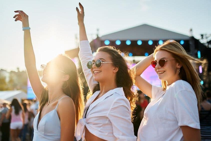 Des filles en robes d'été profitant d'un concert, célébrant avec les mains levées.