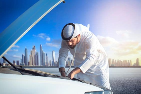 Un homme arabe inspectant sa voiture, capot ouvert.