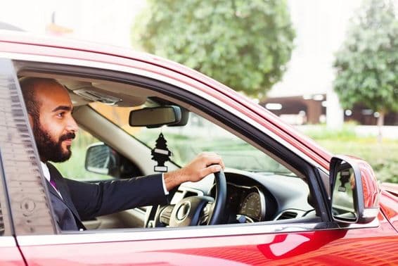 Jeune homme d'affaires conduisant une voiture de location rouge.