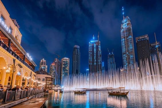 Des personnes en bateau regardant le spectacle de la fontaine de Dubaï la nuit, avec les gratte-ciel de Dubaï en arrière-plan.