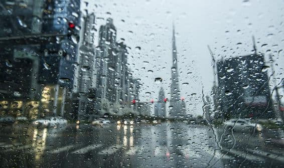 Pluie à Dubaï, vue floue à travers une fenêtre pluvieuse, silhouettes du Burj Khalifa à l'arrière-plan.