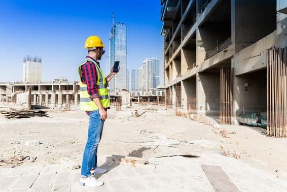 Homme utilisant un smartphone sur un chantier à Dubaï avec la skyline en arrière-plan.