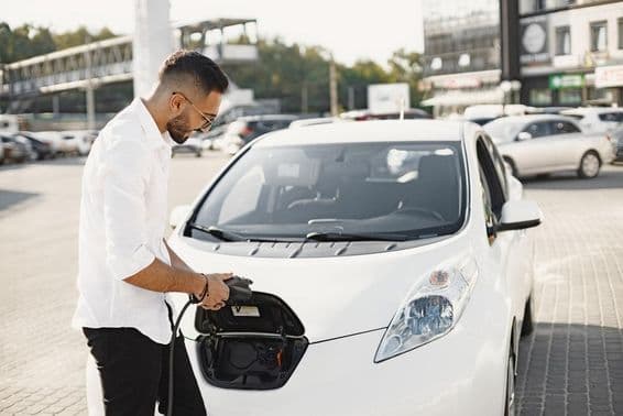 Jeune homme arabe rechargeant une voiture électrique blanche.