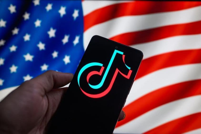 Le logo TikTok affiché sur un smartphone avec le drapeau des États-Unis en arrière-plan.