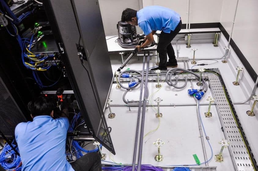 Travailleurs construisant une salle de serveurs, plancher surélevé et armoires de racks.