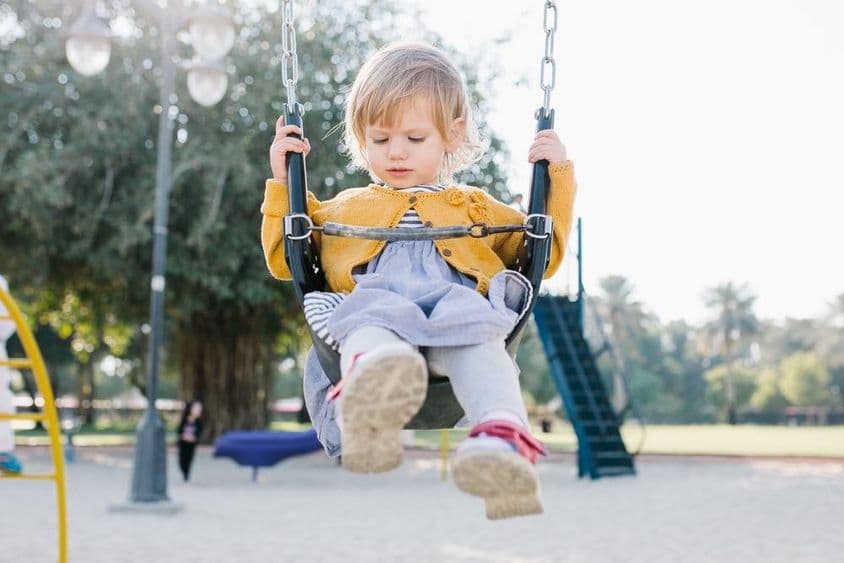 Fille tout-petit heureuse se balançant dans le parc au soleil.