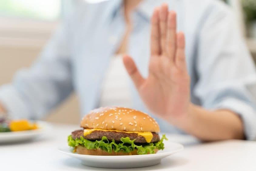 Une femme refuse un hamburger de fast-food riche en graisses.