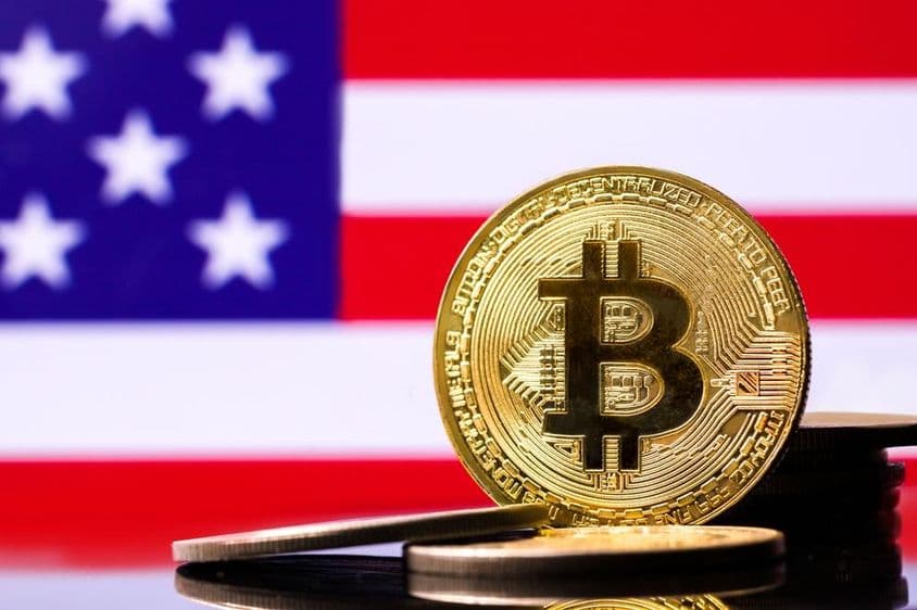 Pièce en métal Bitcoin dorée avec le drapeau des États-Unis en arrière-plan.
