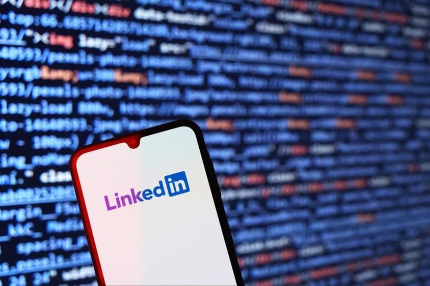 Smartphone affichant le logo LinkedIn avec un extrait de code en arrière-plan.