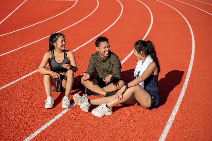Un groupe de sportifs joyeux se reposant sur un terrain de sport sous le soleil après l'entraînement.