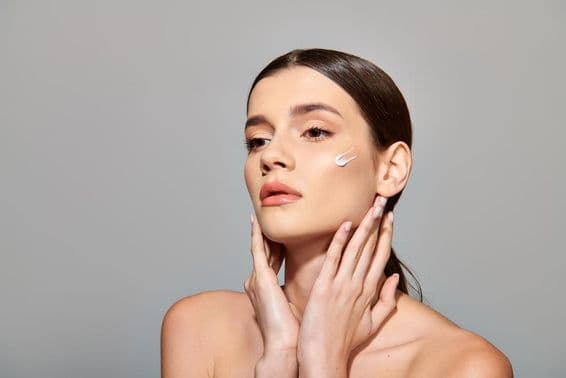 Une jeune femme aux cheveux bruns applique une crème de beauté sur son visage, dégageant un sentiment de soin de soi.