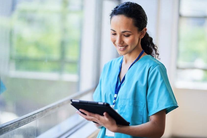 Infirmière souriante avec une tablette numérique dans un établissement médical moderne.
