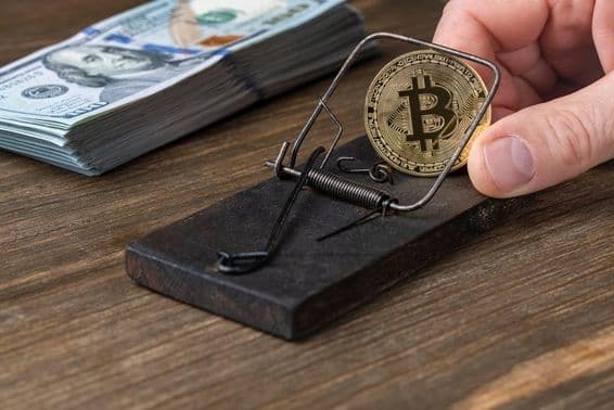 Pièces de monnaie Bitcoin piégées dans une souricière, avec des billets de 100 dollars américains.
