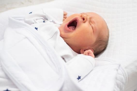 Bébé garçon d'une semaine bâillant sur un lit blanc.
