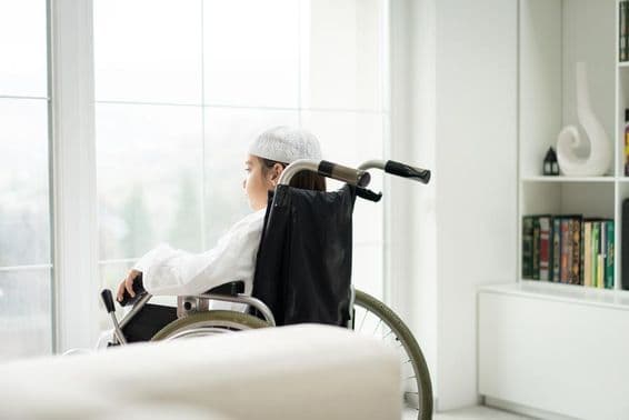 Un jeune garçon en fauteuil roulant regardant par la fenêtre.