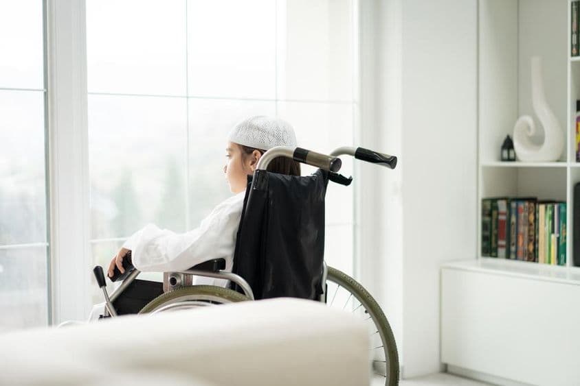 Un jeune garçon en fauteuil roulant regardant par la fenêtre.