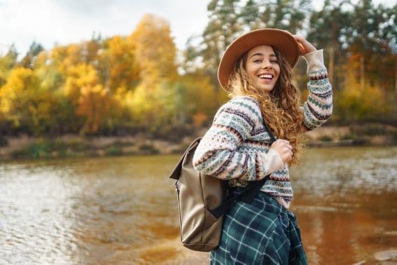 Voyageuse avec sac à dos et casquette profitant d'une randonnée automnale le long d'une rivière.
