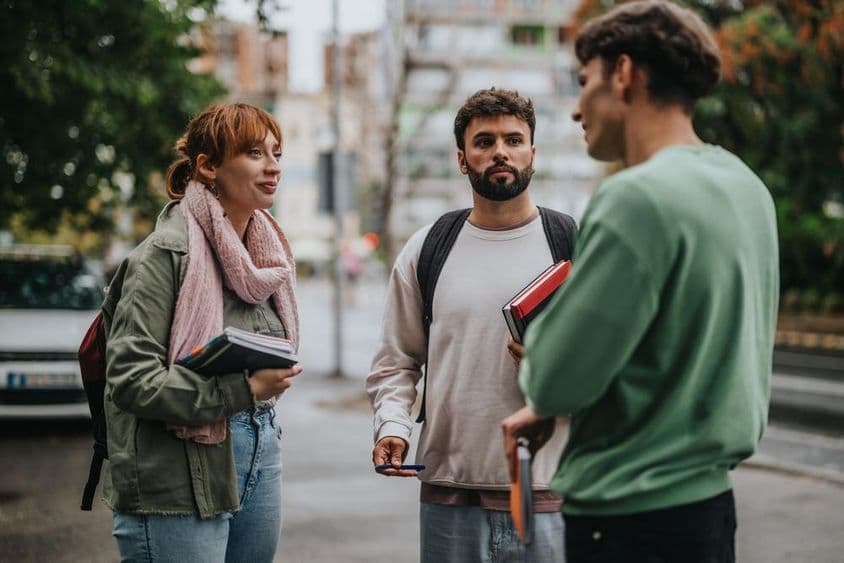 Groupe d'étudiants discutant à l'extérieur avec des livres en main.