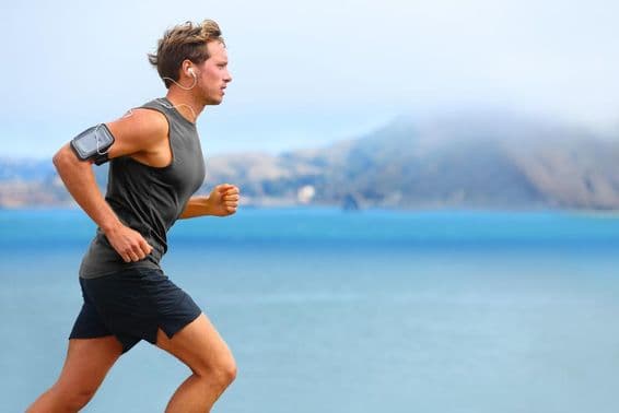 Coureur masculin écoutant de la musique tout en joggant avec un smartphone.