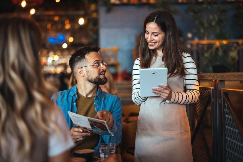 Une serveuse souriante prend une commande dans un bar confortable.