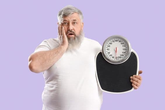 Homme âgé en surpoids choqué tenant une balance en main.