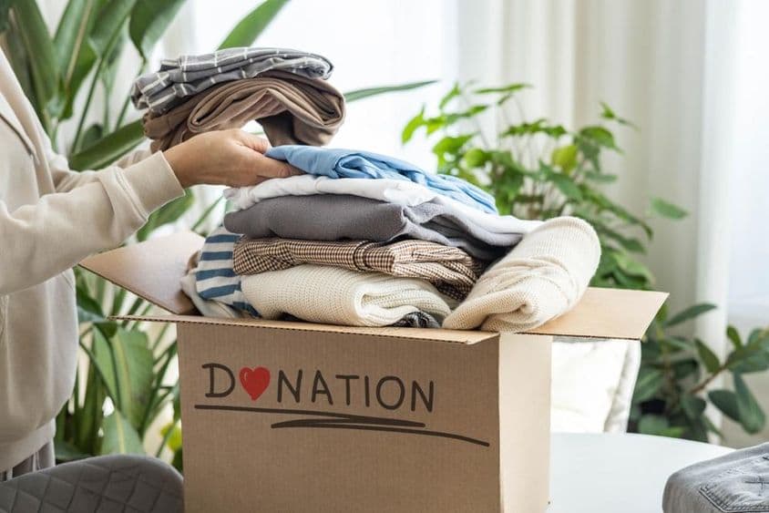 Une femme à domicile plaçant des vêtements dans une boîte en carton pour don, pour recyclage.
