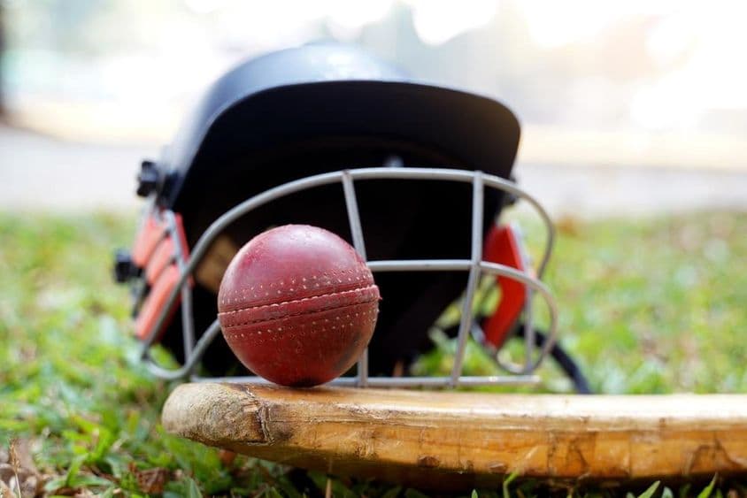 Équipement de cricket avec une balle, une batte et un casque sur l'herbe.