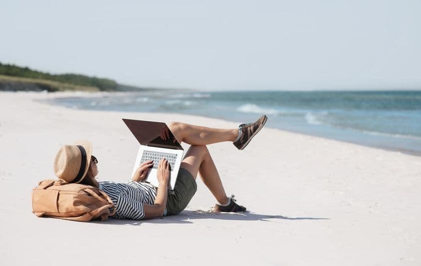 Jeune femme travaillant sur un ordinateur portable au bord de la mer effectuant un travail en freelance.