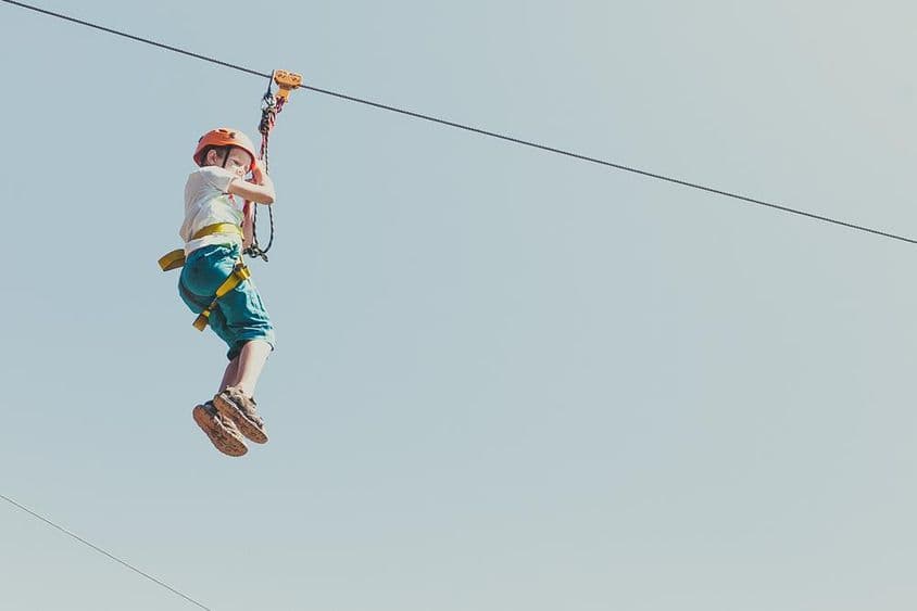 Garçon grimpant dans un parc d'aventures par une journée d'été ensoleillée.