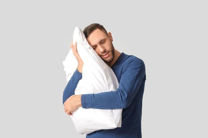 Jeune homme en pyjama avec un doux oreiller.
