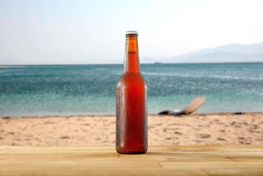 Une bouteille de bière froide sur une table en bois au bord d'une plage de sable.