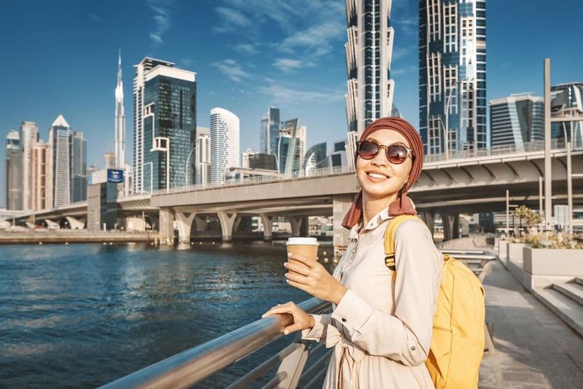Femme musulmane avec un sac à dos jaune marchant près du canal de Dubaï.