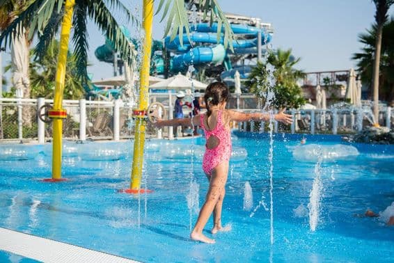 Petite fille jouant dans une piscine avec des fontaines dans un parc aquatique.