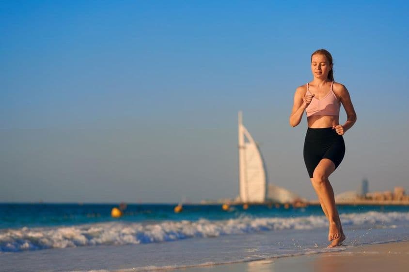 Jeune femme courant sur la plage à Dubaï avec Burj Al Arab Jumeirah en arrière-plan.
