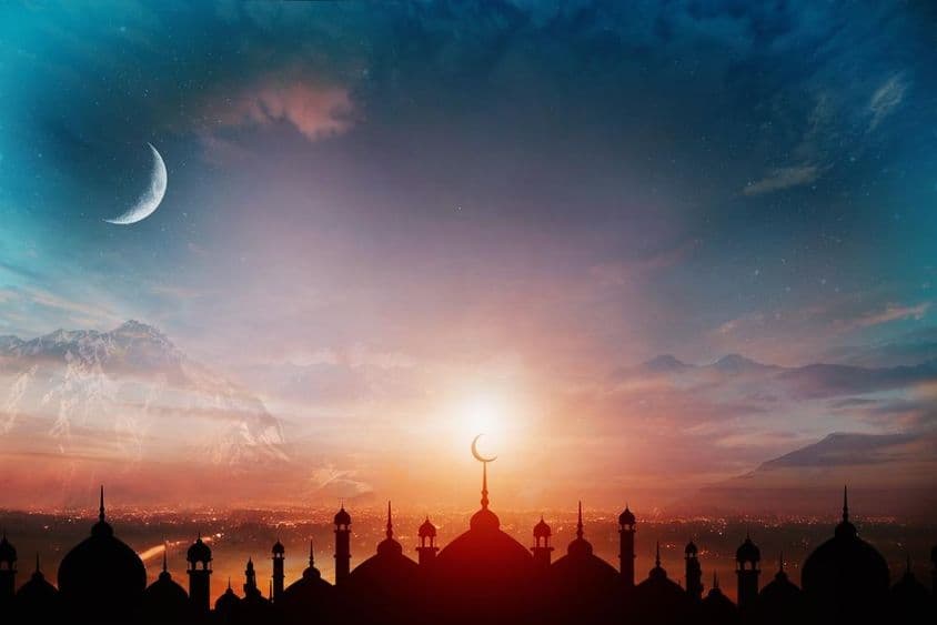 Dômes de mosquée contre un ciel bleu crépusculaire avec un croissant de lune en arrière-plan.