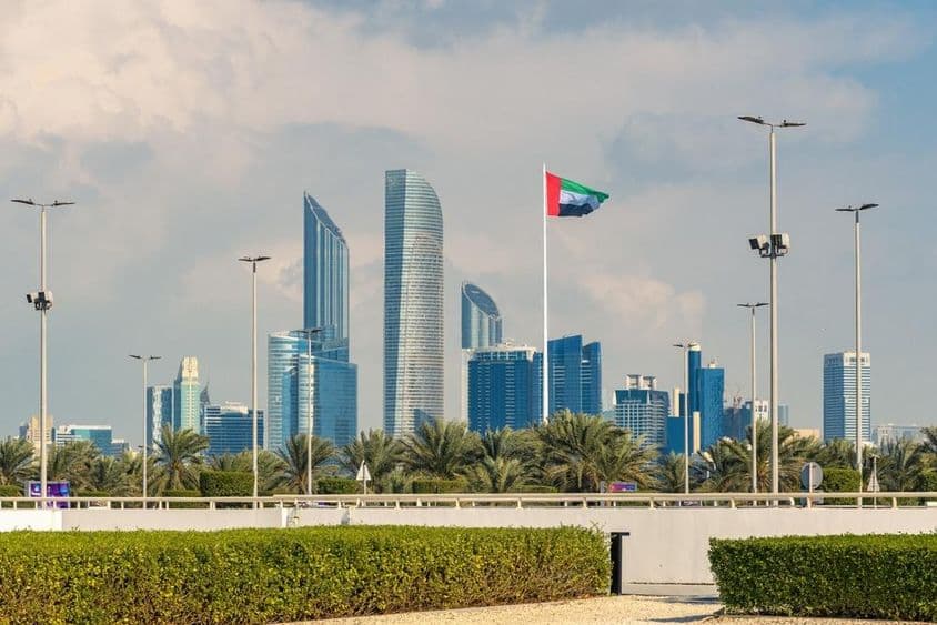 Le skyline emblématique d'Abu Dhabi avec un gratte-ciel moderne et un drapeau national bien visible.