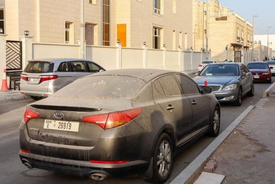 Voitures immatriculées à Dubaï, poussiéreuses et sablonneuses, garées à Abu Dhabi.