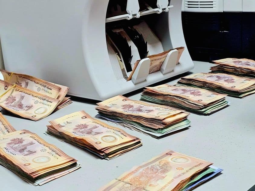 Machine à compter les devises avec des billets de dirhams émiratis bien rangés sur une table