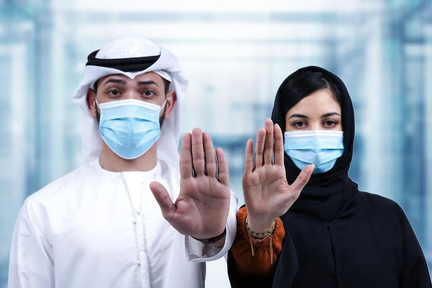 Homme et femme arabes portant des masques médicaux faisant un geste d'arrêt.