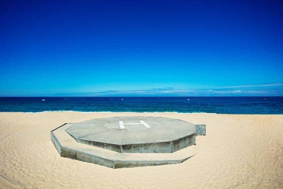 Hélicoptère atterrissant sur une plage de sable à côté d'un océan bleu.