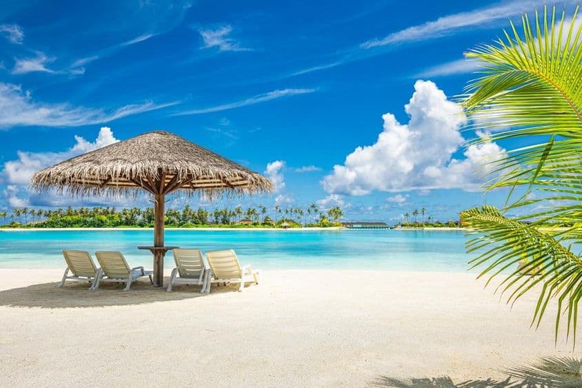 Plage de sable maldivienne avec un parasol et une chaise longue.
