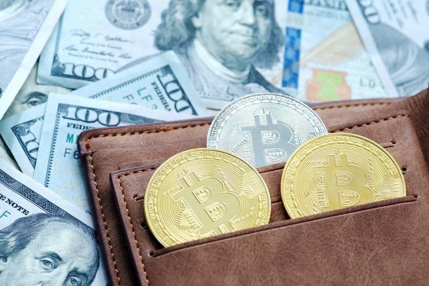 Bitcoin doré avec un portefeuille, sous des billets de dollar.