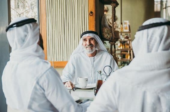 Trois hommes d'affaires prenant le thé à Dubaï en portant des tenues émiraties traditionnelles.