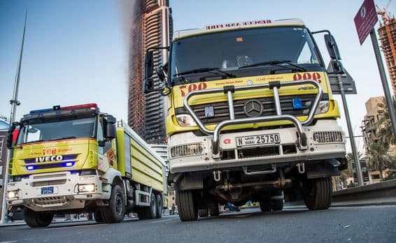 Camions de pompiers de Dubaï garés dans les rues, bâtiment en feu en arrière-plan.