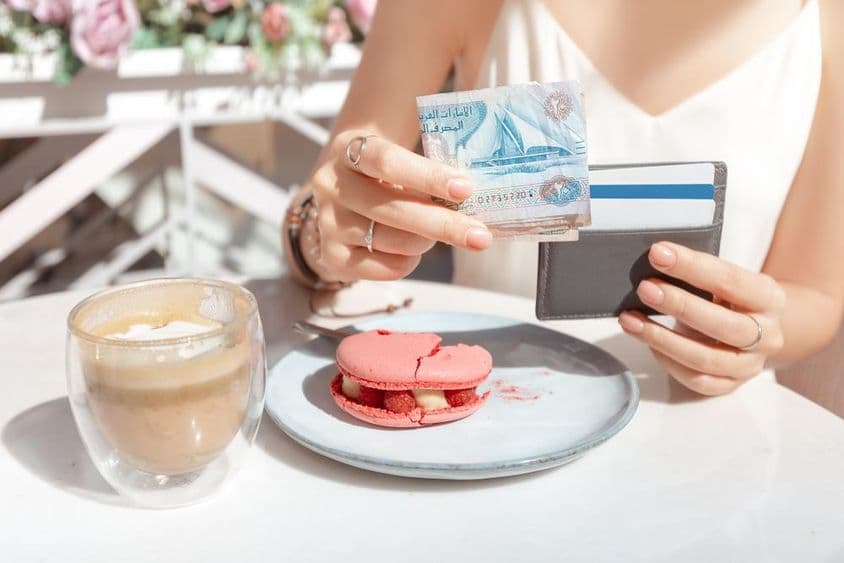 Fille payant son petit-déjeuner dans un café de Dubaï avec des dirhams.