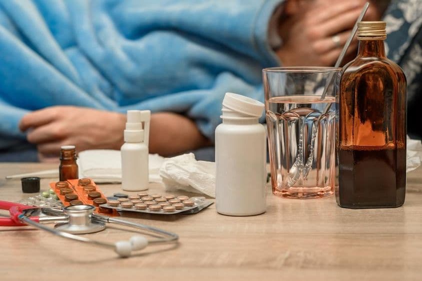 Un homme avec un rhume et de la fièvre allongé au lit.