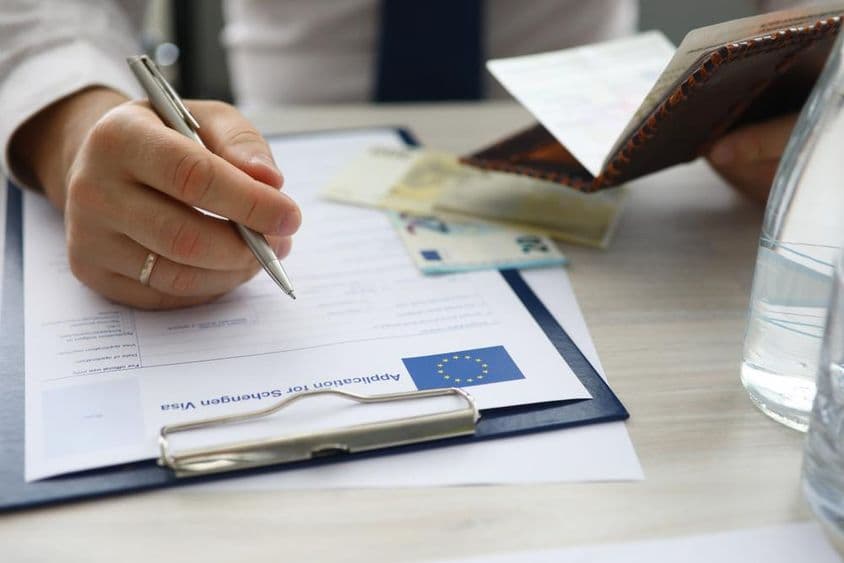 Un homme tenant un passeport et saisissant des informations personnelles sur une demande de visa Schengen.