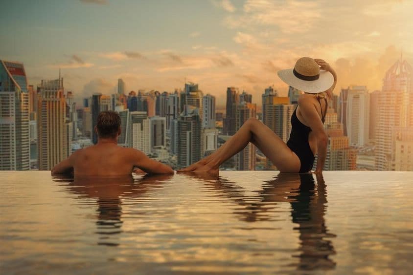 Un couple profite de la vue sur la ligne d'horizon de Dubaï avec son architecture de gratte-ciels depuis une piscine à débordement au coucher du soleil.